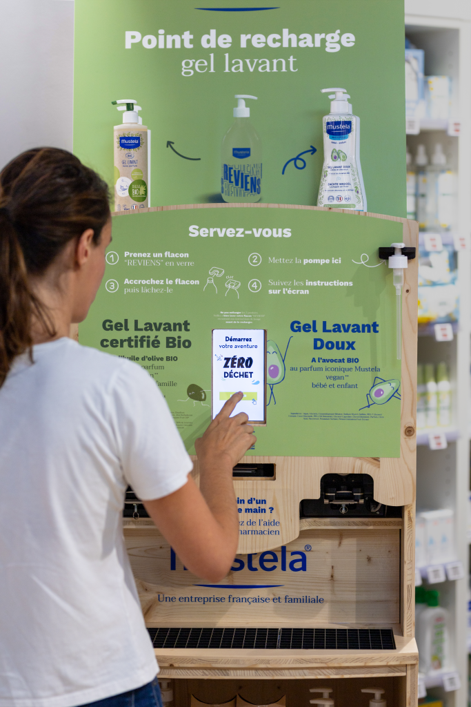 Une cliente recharge son flacon en gel lavant Mustela en pharmacies en naviguant sur l'écran de la fontaine vrac